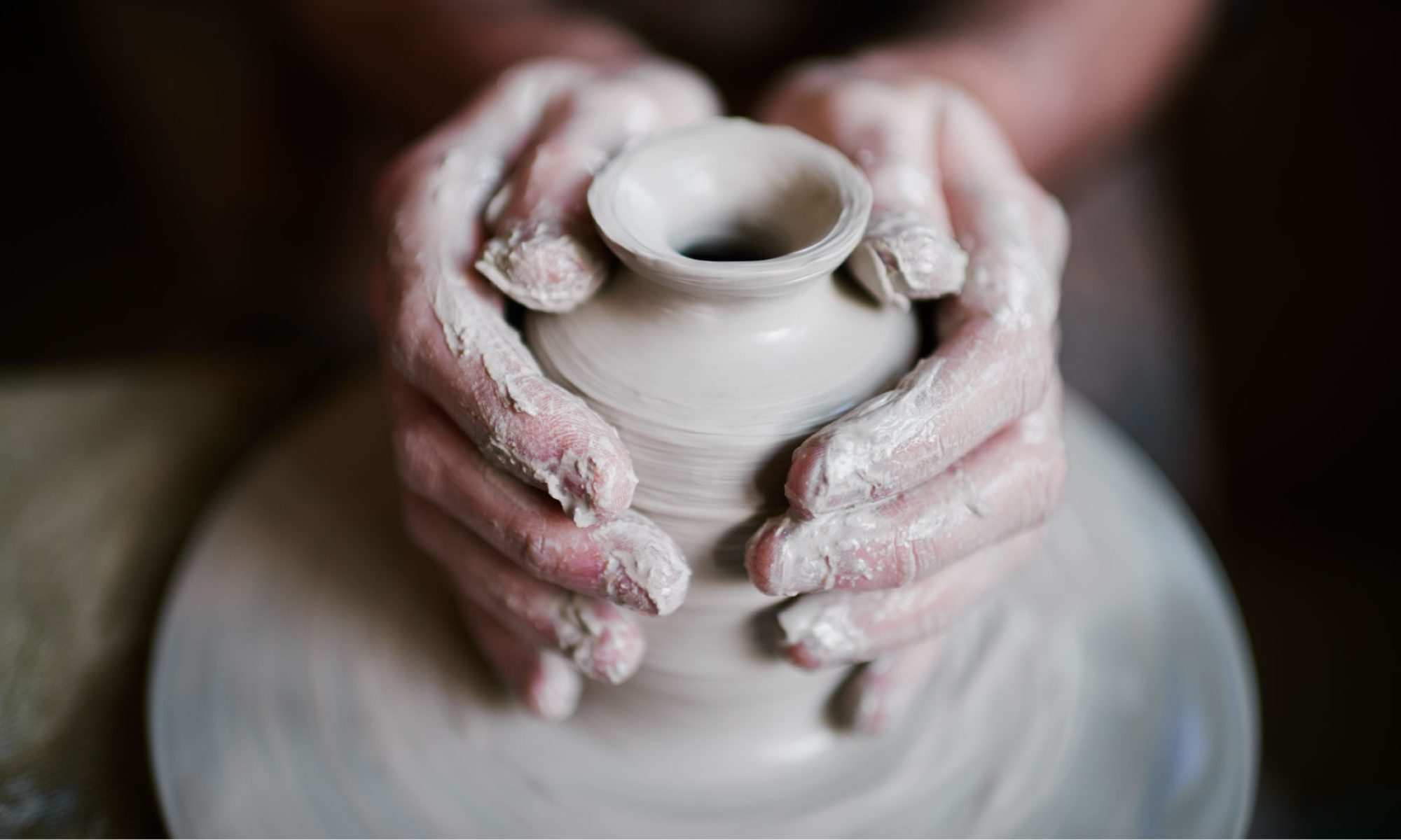 The image shows the hands of a potter forming clay into a vase.